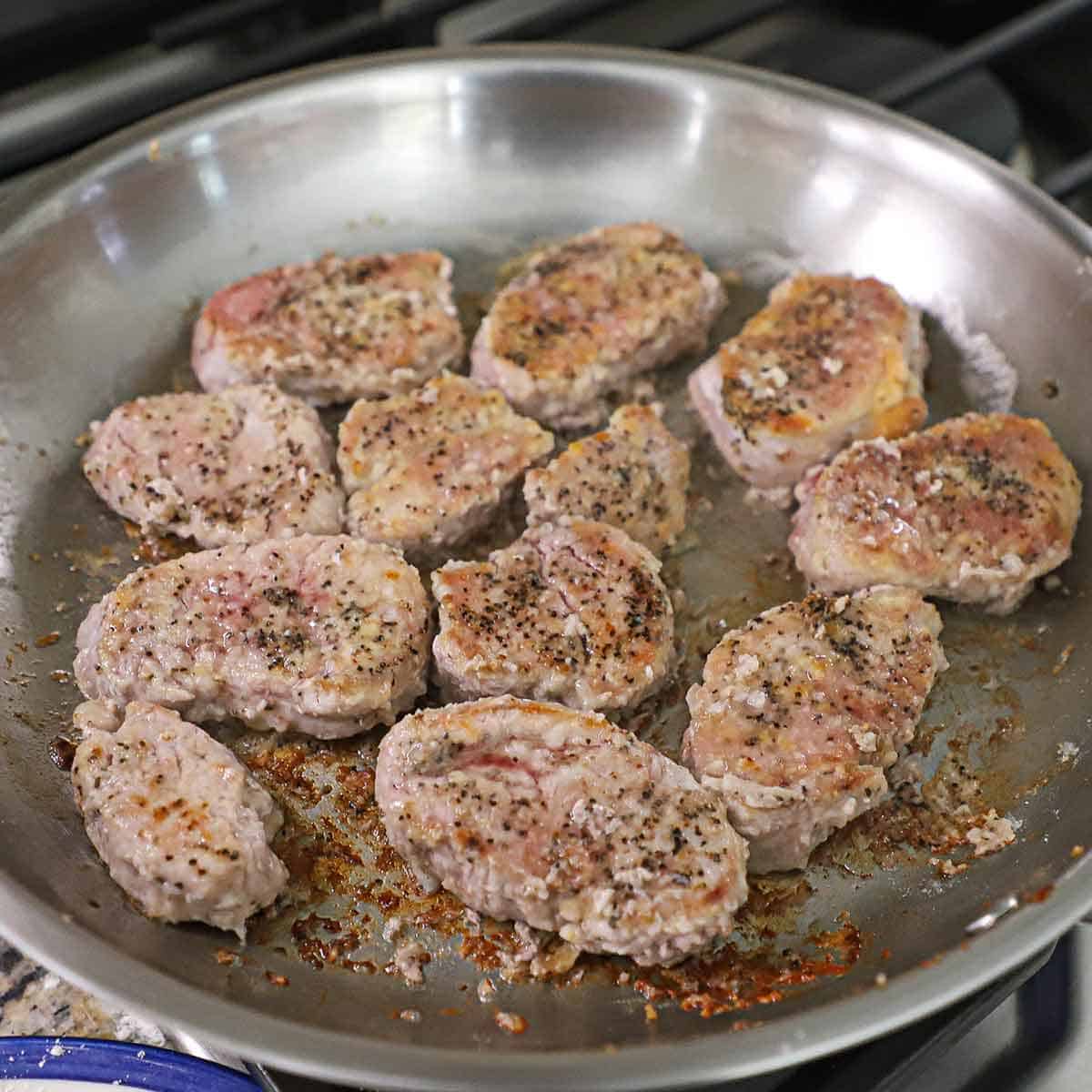 A skillet filled with lightly breaded pork medallions that are being seared and browned in hot olive oil and melted butter.