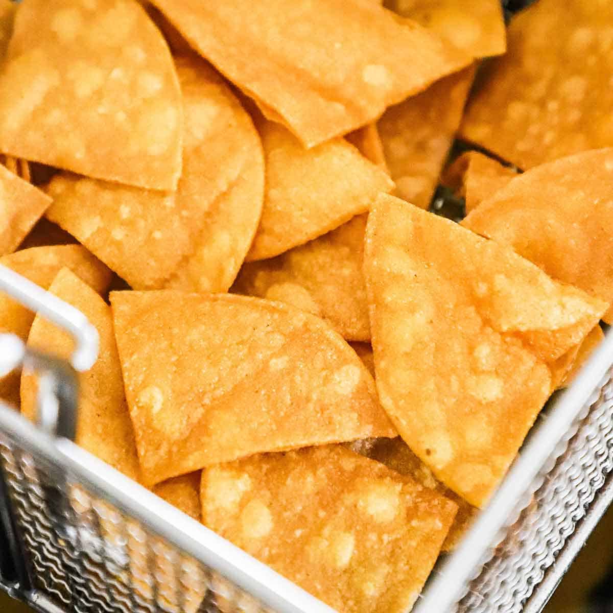 A close-up view of freshly fried tortilla chips in a fryer basket.