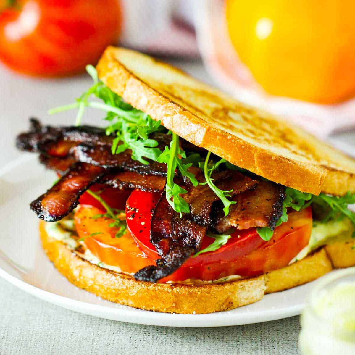 A close-up view of a Classic BLT with Garlic Basil Aioli on lightly toasted sourdough bread on a white plate.