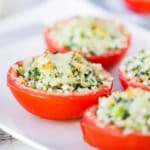 A close-up view of four Baked Stuffed Summer Tomatoes with lightly browned cheese and breadcrumbs on the top of the tomatoes.