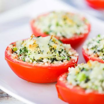 A close-up view of four Baked Stuffed Summer Tomatoes with lightly browned cheese and breadcrumbs on the top of the tomatoes.