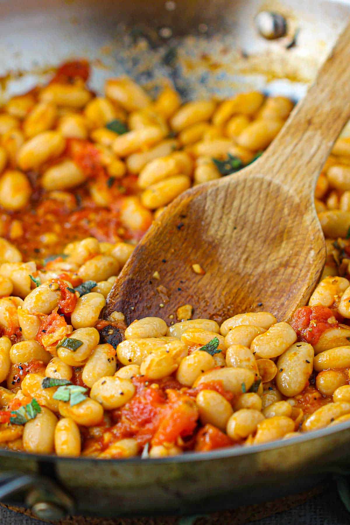 A straight-on view of a large silver skillet filled with freshly prepare Sautéed White Beans with Garlic, Sage, and Tomatoes.