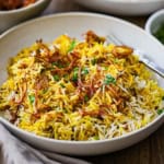 A straight-on view of a shallow bowl filled with a serving of Hyderabadi Chicken Biryani topped with fried onions and chopped cilantro.