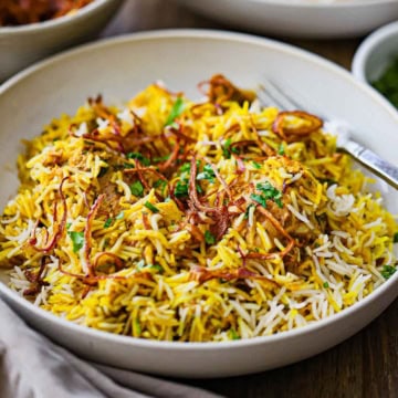 A straight-on view of a shallow bowl filled with a serving of Hyderabadi Chicken Biryani topped with fried onions and chopped cilantro.