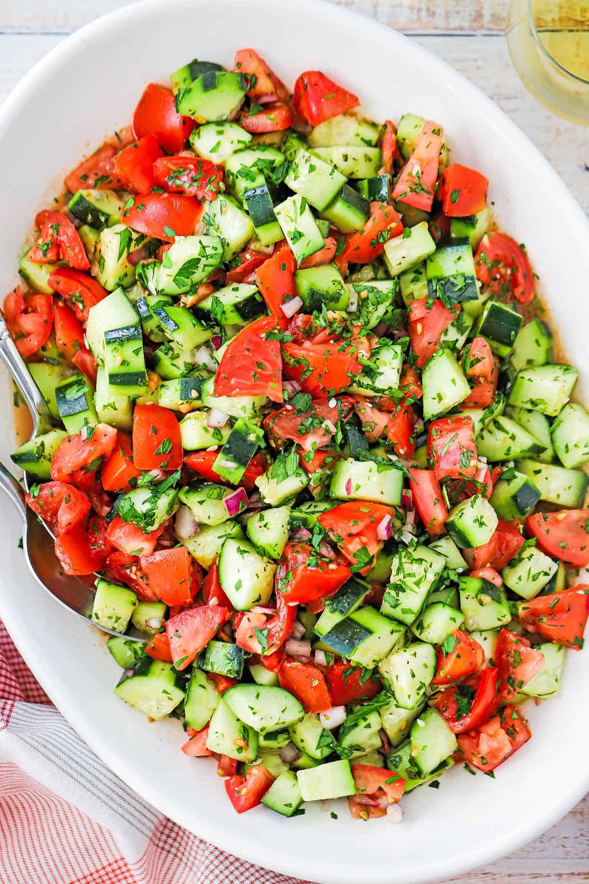 An overhead view of a large oval platter filled with a Chopped Cucumber Tomato Salad topped with fresh herbs.