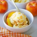 A white ice cream bowl filled with several scoops of homemade peach ice cream with a orange checkered napkin nearby.