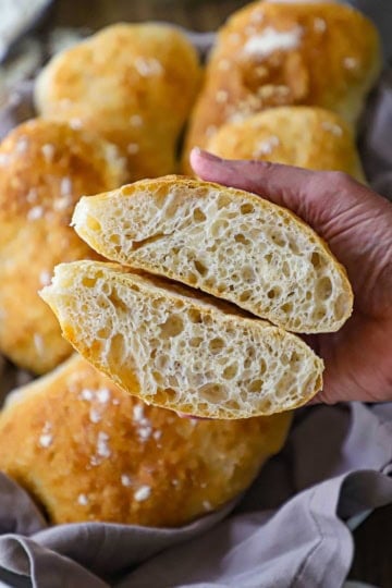 A person holding two halves of a homemade ciabatta bun that has been split in half and the inside with large air pockets are visible.