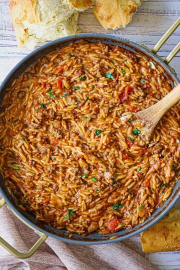 An overhead view of Cheesy One-Pot Ground Beef Orzo in a large skillet with a large wooden spoon inserted in the side of the dish.