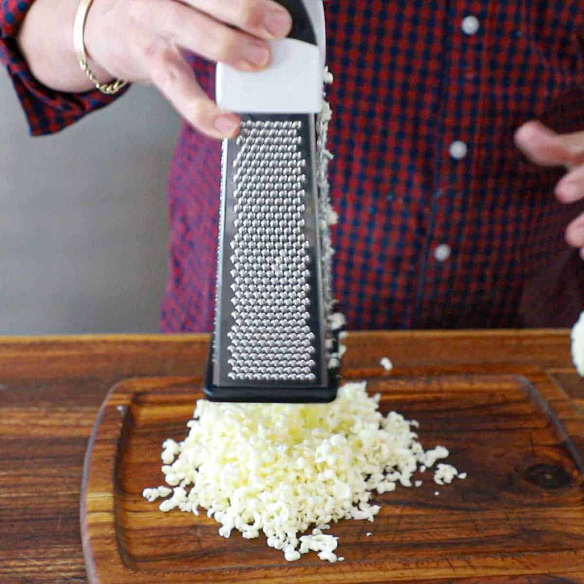 A person lifting a box grater from a wooden cutting board revealing a freshly grated pile of cold butter.