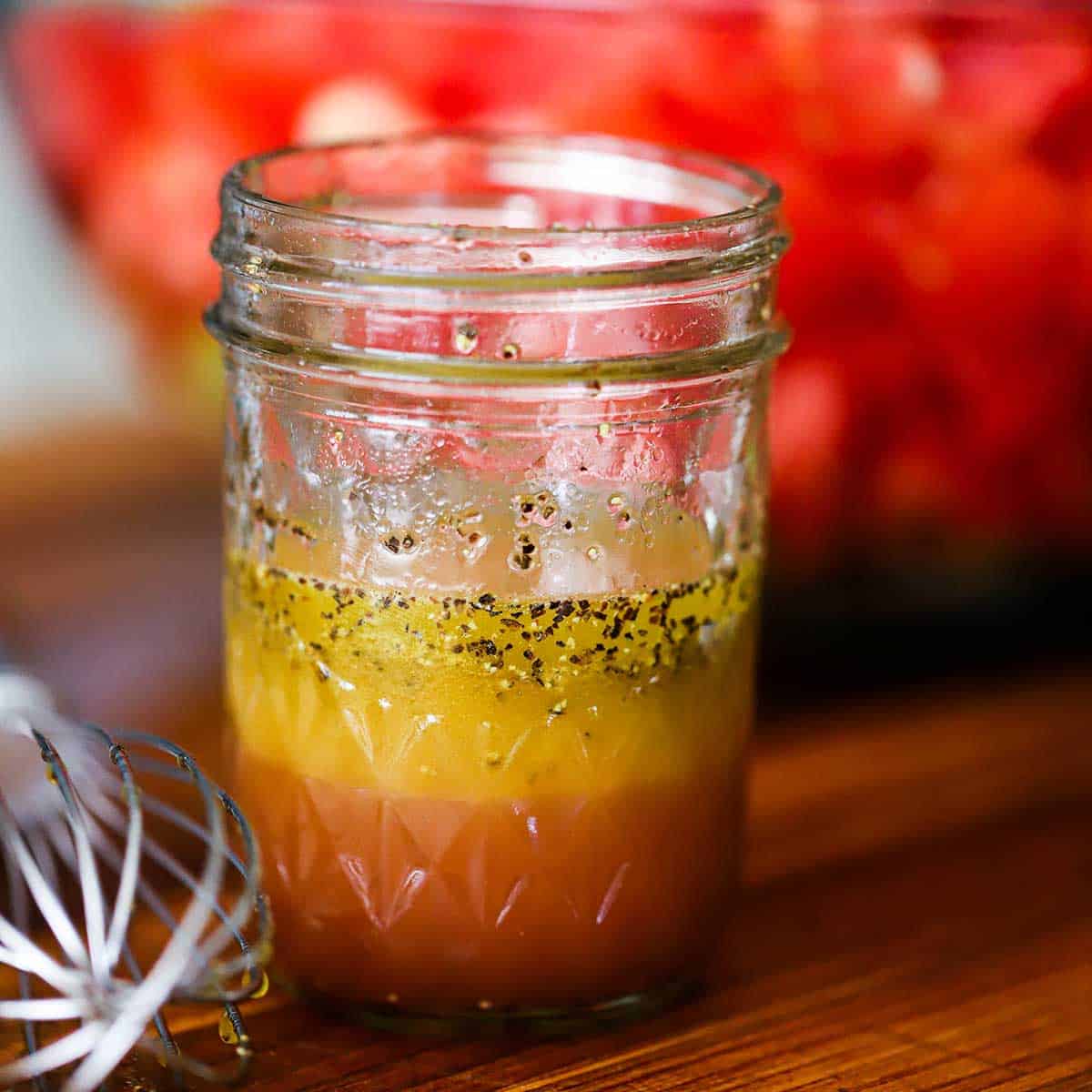 A straight-on view of a small glass jar filled with a red wine vinegar and apple cider vinegar vinaigrette.