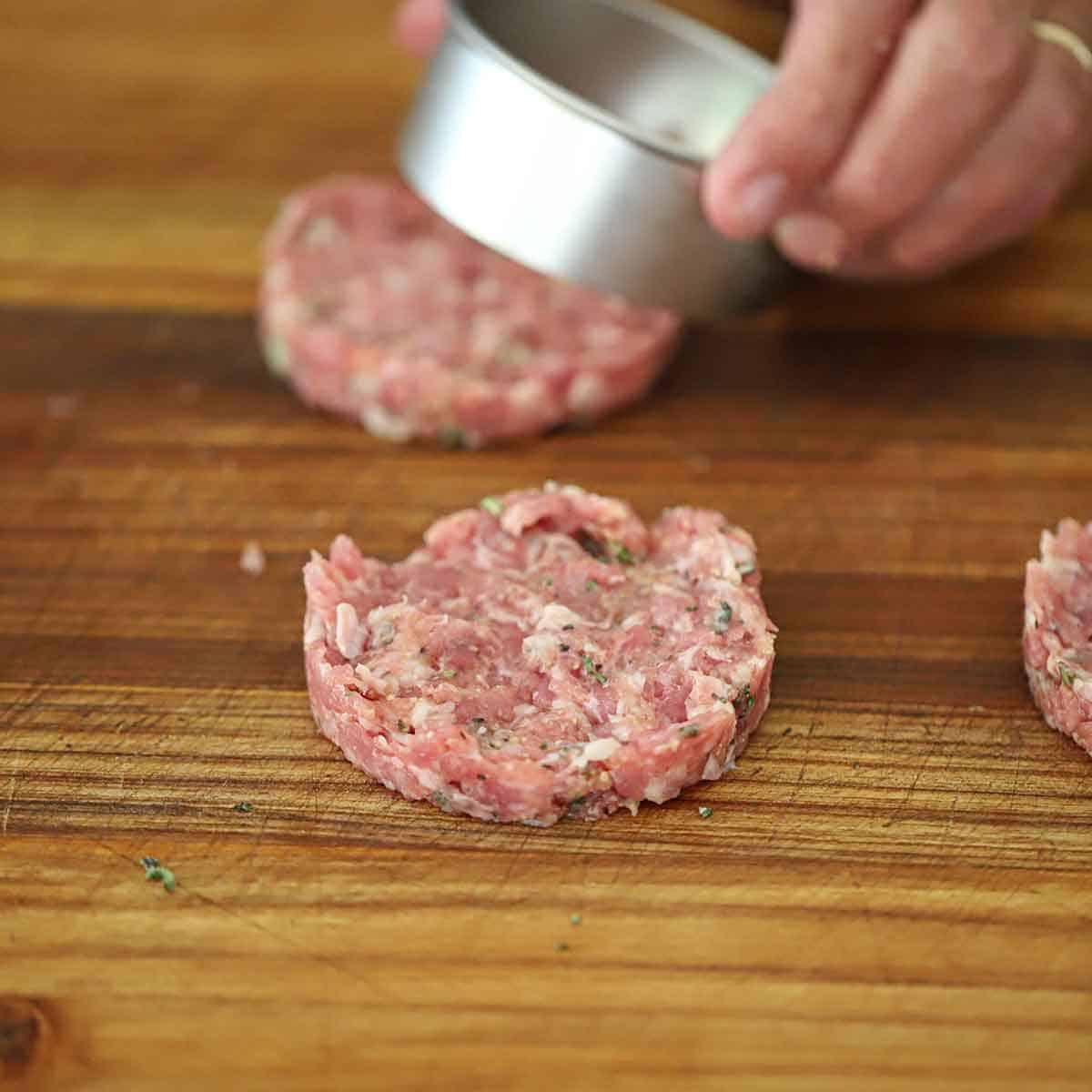 A person using a metal ring to form an uncooked maple sausage patty on a wooden cutting board.
