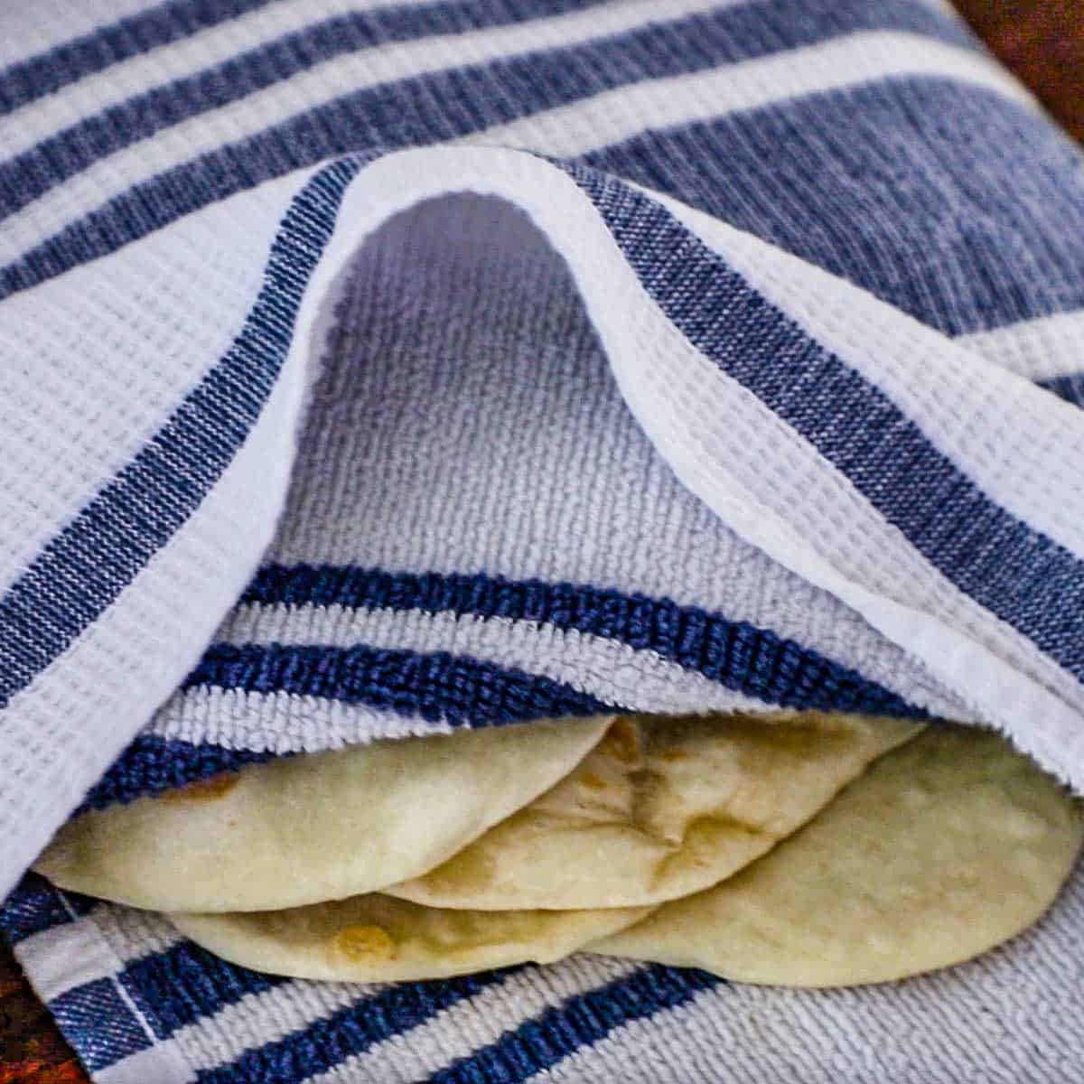 A straight-on view of the ends of stack of homemade garlic naan that is nestled in between a white and blue kitchen towel.