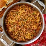 An overhead view of a large skillet that is filled with spaghetti bolognese that is garnished with chopped Italian parsley.