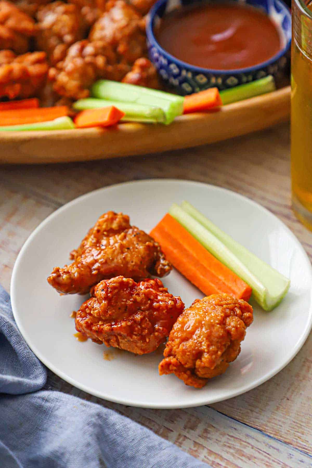 A small white cocktail plate with three boneless chicken wings and a stalk of celery and carrot all resting on it.