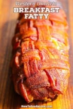 A straight-on view of a fully cooked smoked Western omelette Fatty that has been encased in a season bacon weave and is resting on a wooden cutting board.