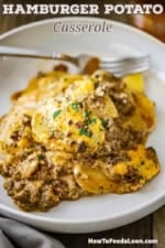 A serving of hamburger potato casserole piled high in a shallow bowl with a fork in the background.