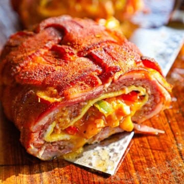 A close-up view of a smoked Western omelette fatty that has been cut in half revealing the melty cheddar cheese, sautéed vegetables, cooked eggs, and juicy sausage, all wrapped in a seasoned bacon weave.