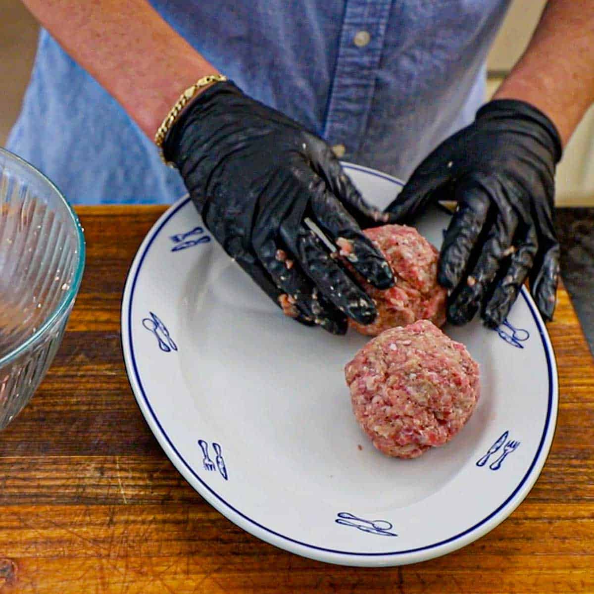 A person placing rolled large uncooked Dutch meatballs on a large oval platter.