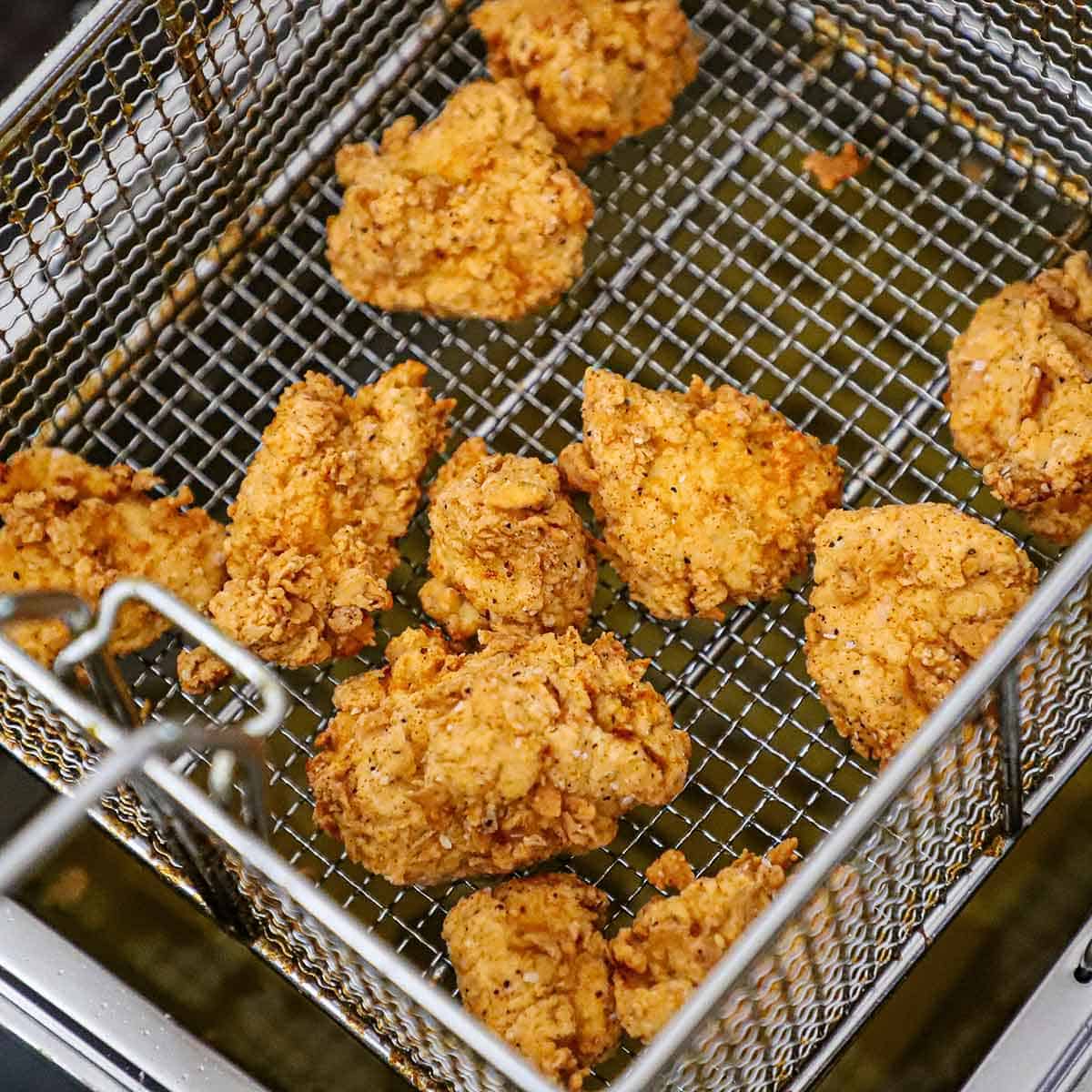 A close-up view of crispy boneless chicken wings resting a metal basket over the top of a deep-fryer.